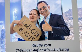 Zwei Personen sind lachend hinter einem weißem Bildrahmen mit der Aufschrift: Grüße vom Thüringer Außenwirtschaftstag