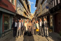 Internationale Delegation bei einem gemeinsamen Rundgang durch die historische Altstadt von Erfurt. Rund zwölf Teilnehmende einer mexikanischen Delegation posieren in einer schmalen Fachwerkgasse zwischen Geschäften und Gastronomiebetrieben.