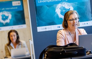Zwei Frauen befinden sich in einer Video-Konferenz. In der Mitte der Beiden ist ein Raumtrenner.