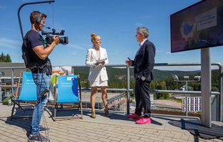Die Moderatorin spricht mir einem Mann unter offenem Himmel. Ein Kameramann film sie dabei.