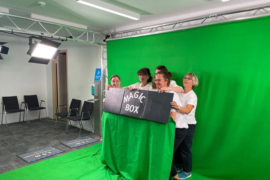 Vier Personen posieren vor einem Green-Screen und lächeln in die Kamera.