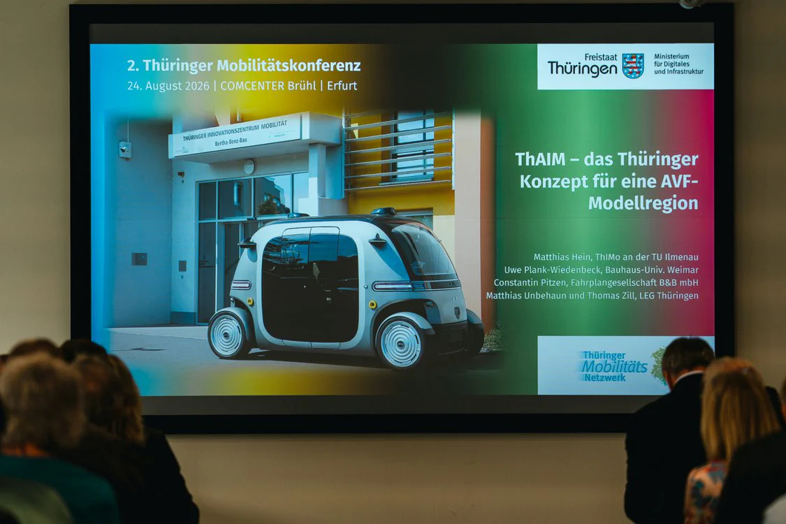 Copyright: TMDI / B. Schmidt Presentation slide for the Thuringia Mobility Conference about the ThAIM project with an autonomous shuttle vehicle and speakers from science and practice