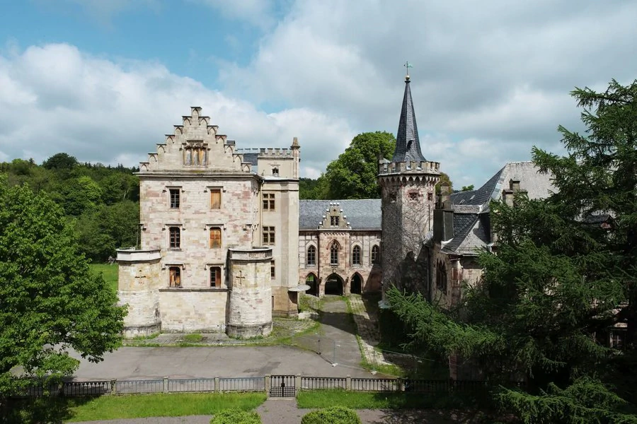 Luftaufnahme Schloss Reinhardsbrunn Luftaufnahme eines Schlosses mit einem Turm und einem Innenhof, umgeben von grüner Landschaft.