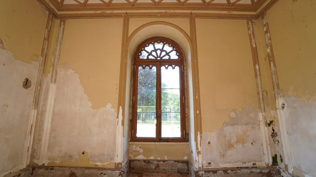 Innenaufnahme vom Schloss Reinhardsbrunn Ein Raum mit einem Fenster und einer Wand, deren Farbe abblättert, vermittelt einen Eindruck von Verfall und Vergänglichkeit.
