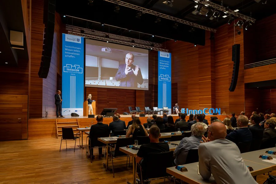 InnoCON Bildergalerie Ein großer Hörsaal mit einer großen Leinwand, die eine Präsentation zeigt.