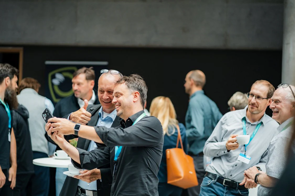 Teilnehmende des Maschinenbautags 2026 tauschen sich in einer Networking-Pause aus und machen ein Foto mit einem Smartphone.