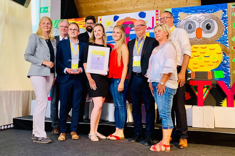 Eine Gruppe von Personen steht auf der Bühne und hält stolz ein Zertifikat in den Händen.