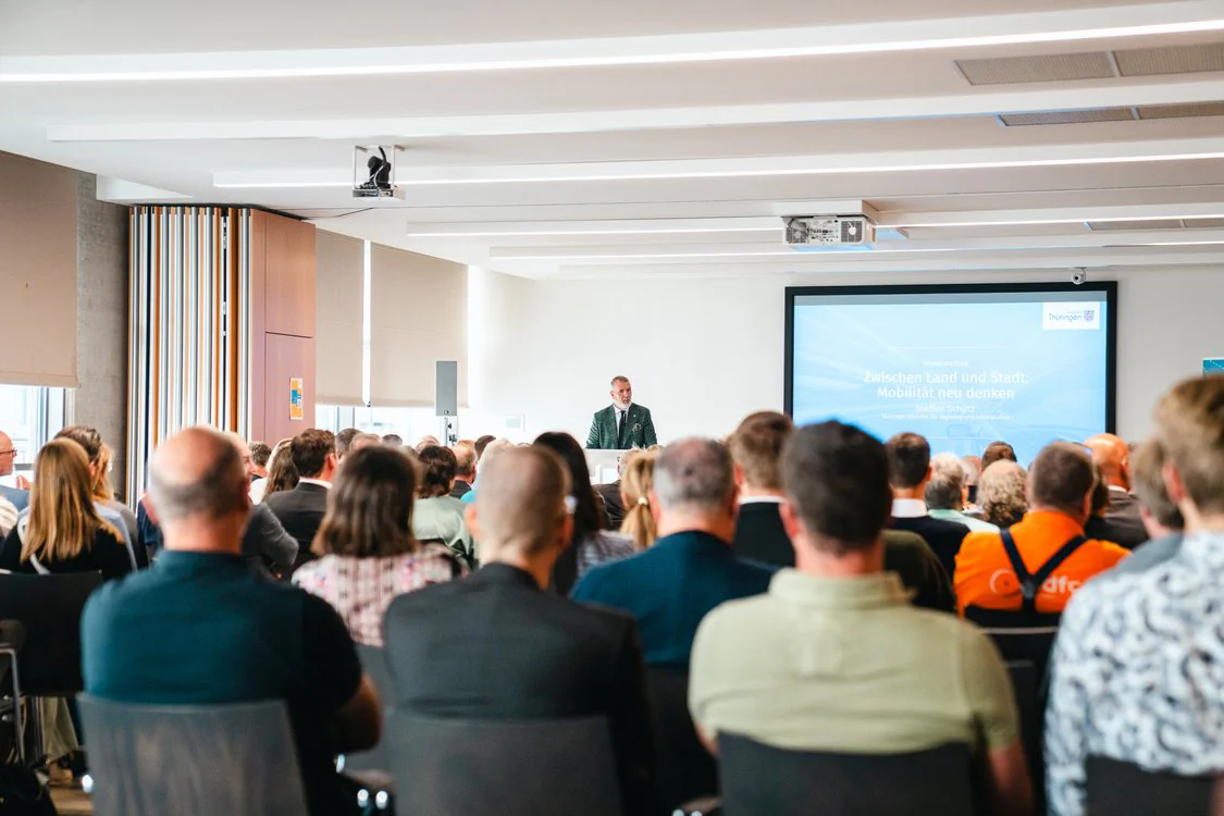 Copyright: TMDI / B. Schmidt Conference room with a large audience during a presentation. A speaking person stands at the lectern in front of a large presentation slide, while the participants look at the stage.