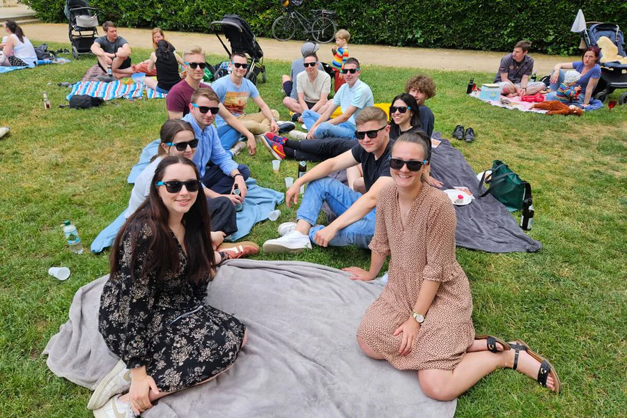 Eine Gruppe von Menschen sitzt auf einer Decke im Gras und genießt die Zeit im Freien.