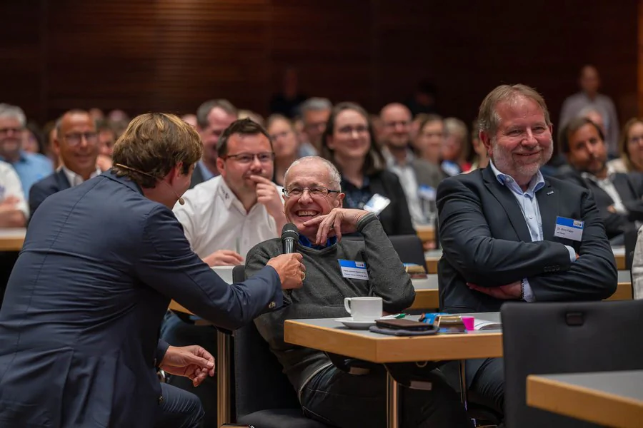InnoCON Bildergalerie Der Keynote Sprecher unterhält sich mit einer lachenden Person im Publikum