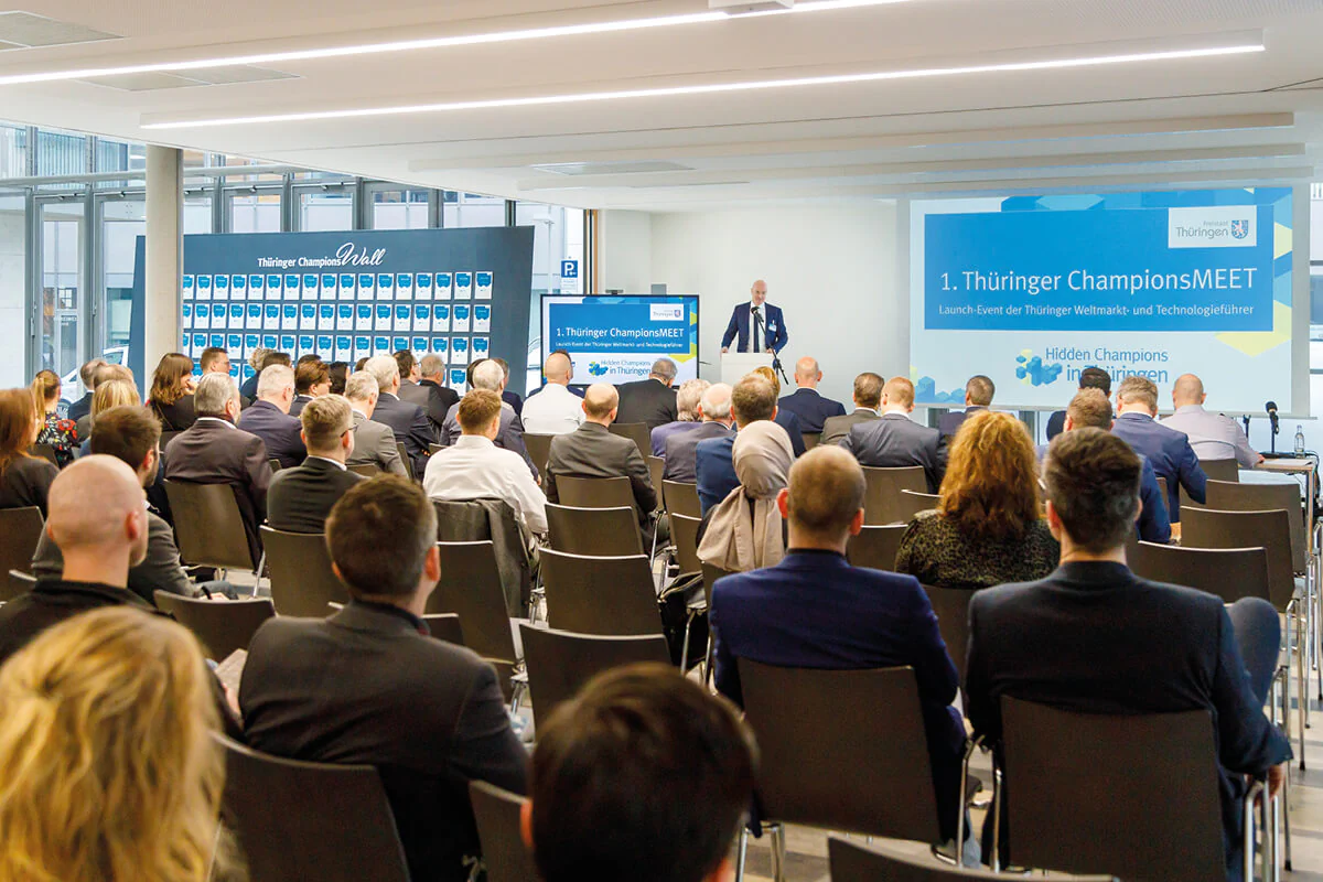 Bildbeschreibung / description: Eine große Gruppe von Menschen hört einer Person zu, die eine Rede hält. Event: ChampionsMEET